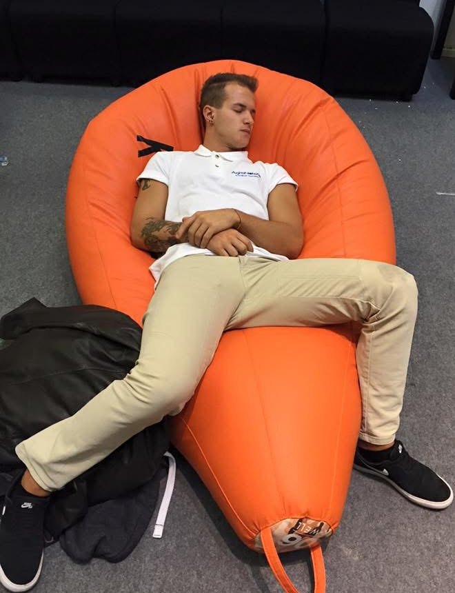 David Valmori addormentato su un pouf arancione, di giorno, con lo zaino a terra